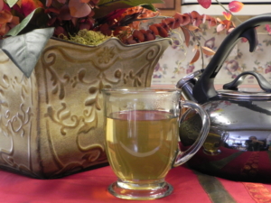ESSIAC TEA IN A CUP SITTING ON A TABLE WITH A TEA POT AND VASE WITH FLOWERS