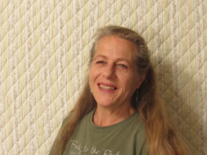 INGRI CASSEL SMILING WITH LONG HAIR WEARING A GREEN SHIRT IN FRONT OF QUILTED BACKGROUND