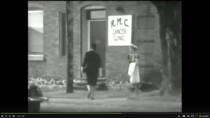 FRONT DOOR TO THE RENE M. CAISSE CANCER CLINIC IN BRACEBRIDGE, ONTARIO IN THE 1930S. WOMAN IS WALKING TOWARD THE FRONT DOOR WITH SIGN NEXT TO THE DOOR STATING; 